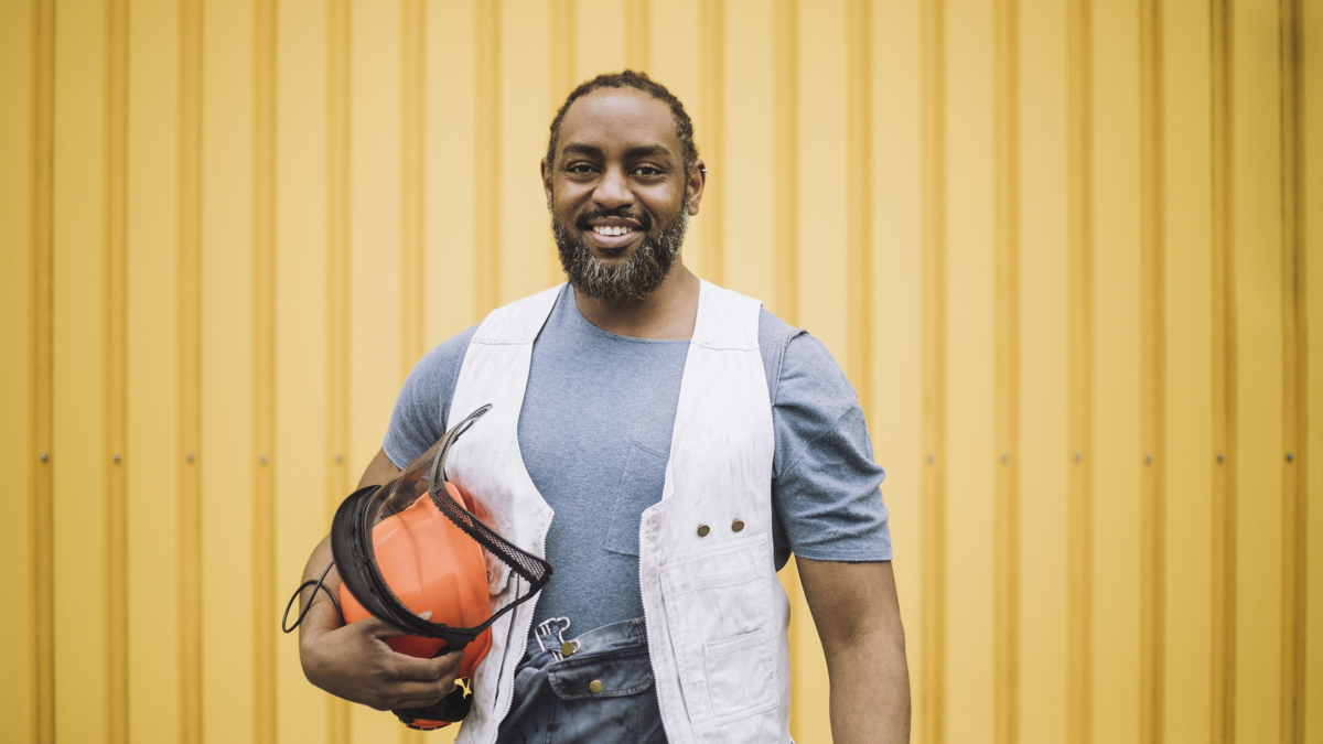 En glad man med en skyddshjälm under armen ler mot kameran.