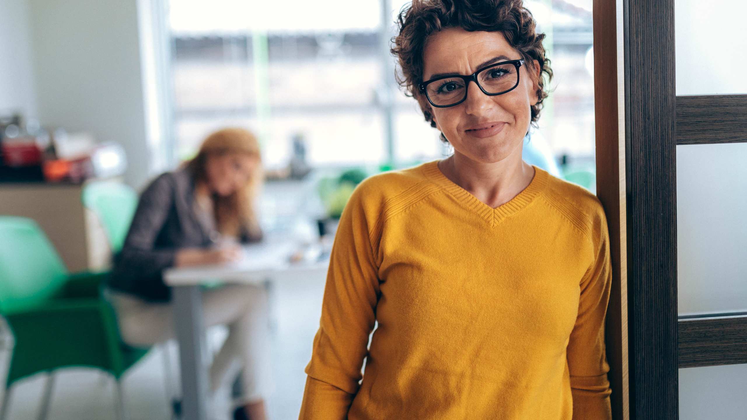 Mörkhårig kvinna i orange tröja tittar in i kameran